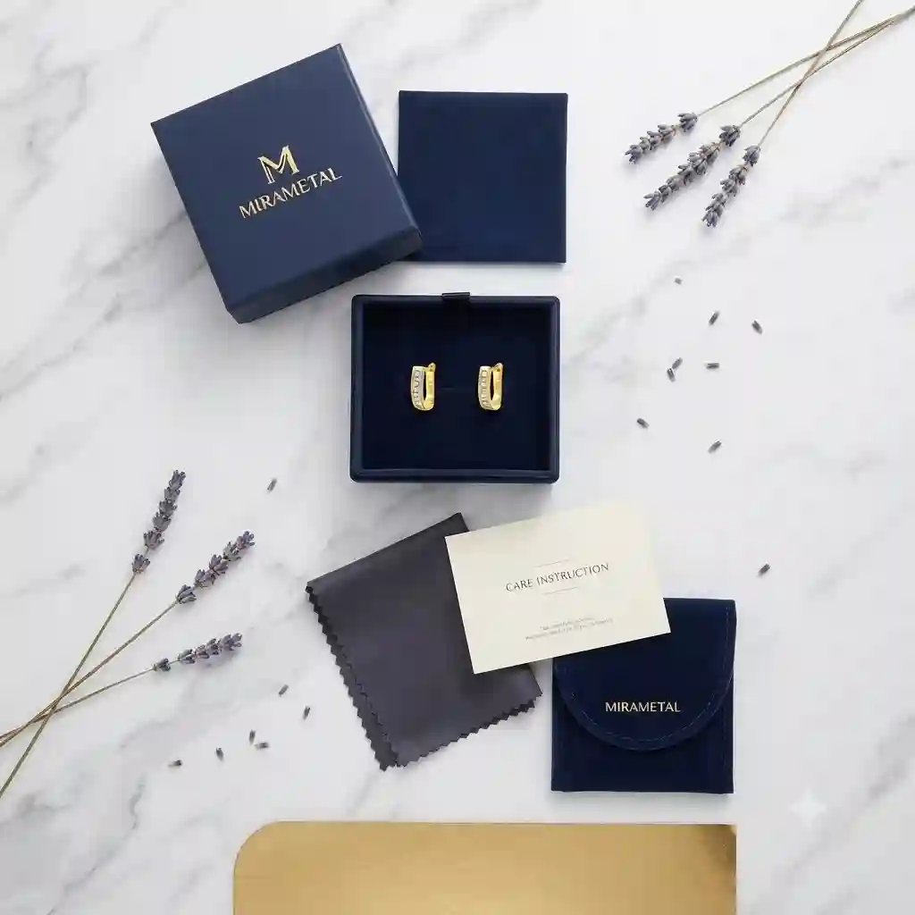 Complete MIRAMETAL luxury unboxing of U-shape channel-set zirconia ear cuff: navy velvet gift box, polishing cloth, care card, brand pouch, four CZ stones gleaming on marble surface