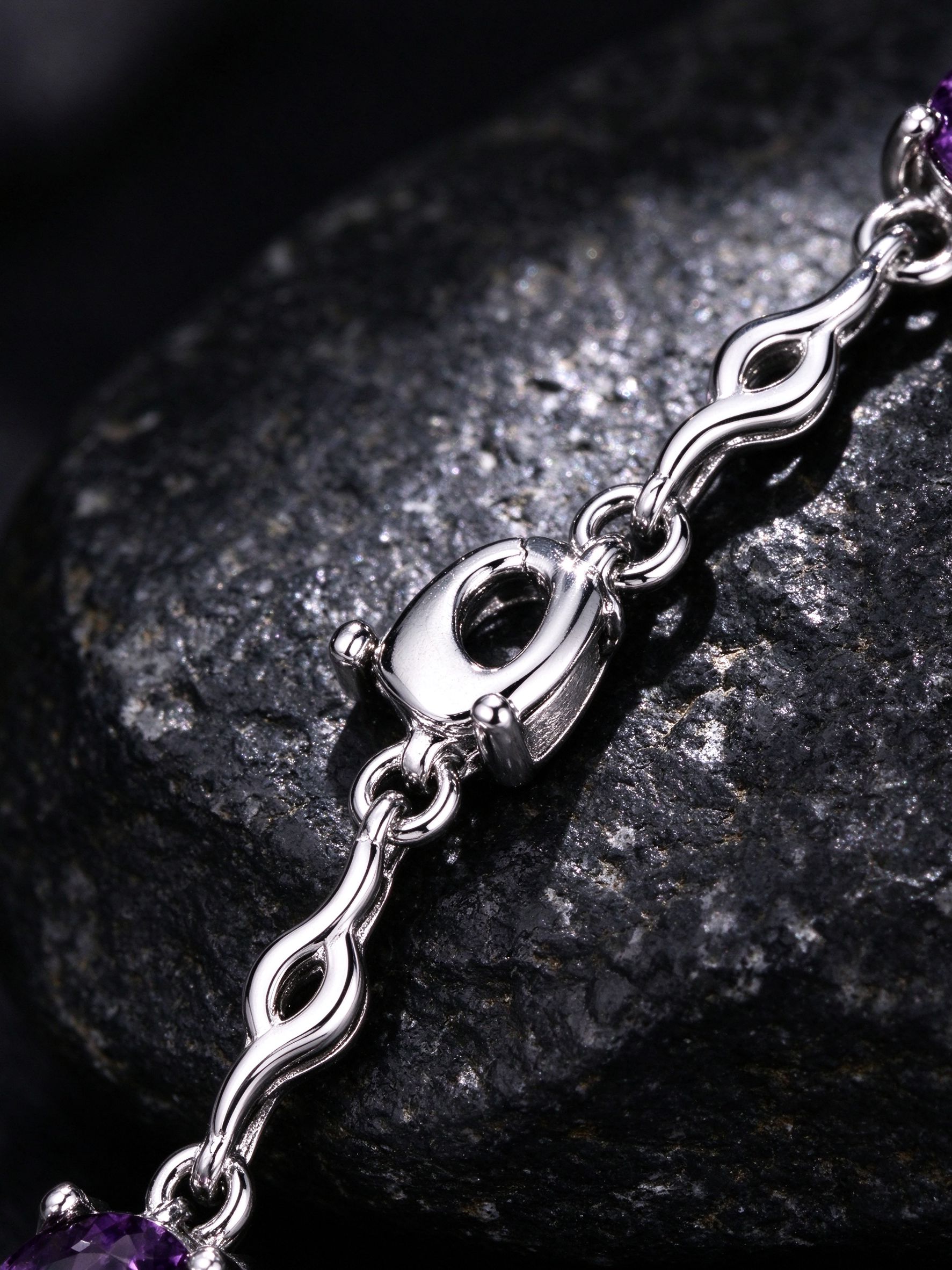 Close-up of wavy infinity chain links and prong setting on amethyst bracelet, rhodium silver finish